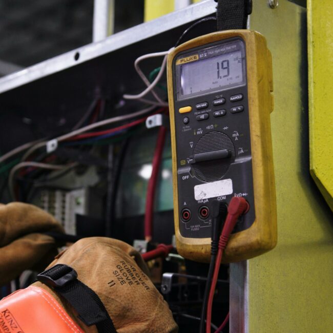 Electrician using a multimeter to fix industrial control panel wiring.