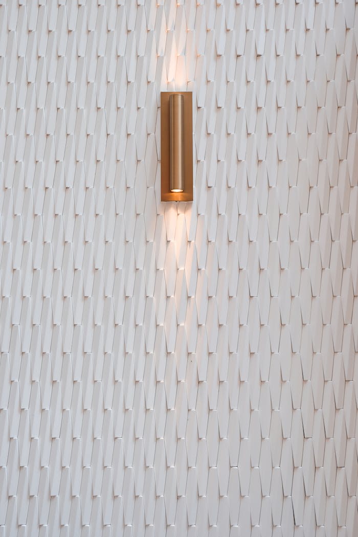 Elegant wall light fixture on textured white wall, showcasing modern minimalist decor.