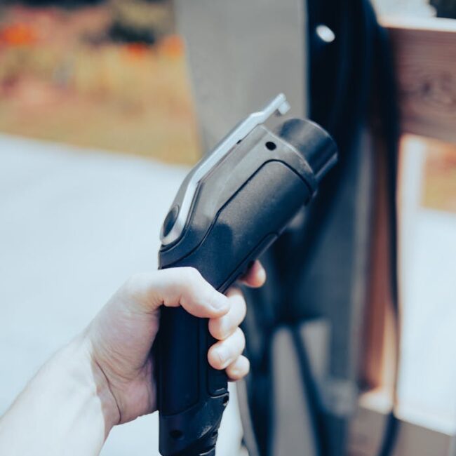 Close-up of a hand holding an EV charging cable outdoors, highlighting modern technology.